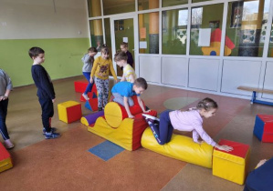 Dzieci bawią się na torze przeszkód ułożonym w sali gimnastycznej